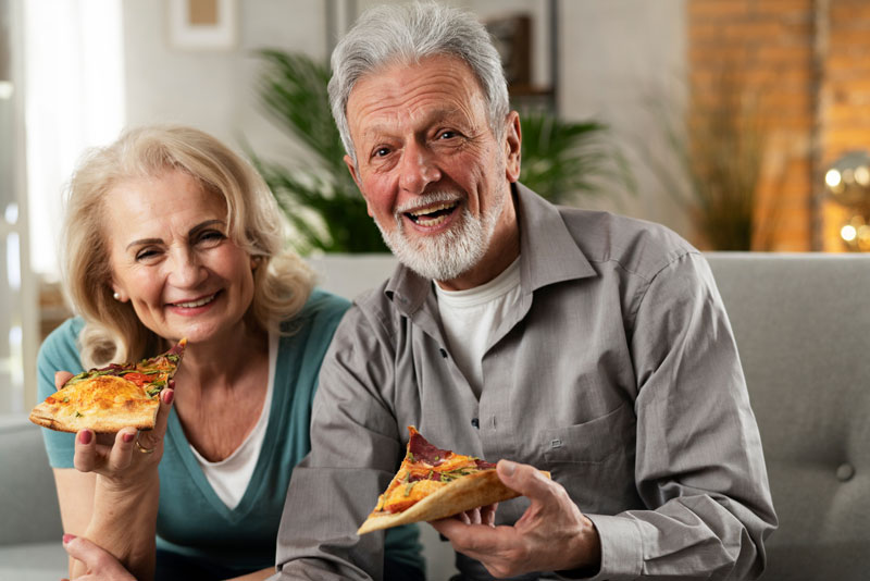 two implant supported denture patients smiling and eating.