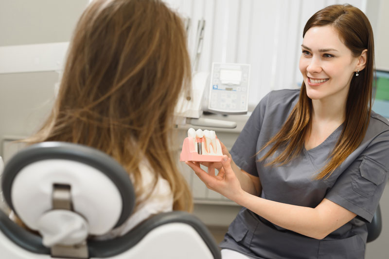 a dental professional holding up a dental implant model to show the patient why they should get treated with tooth implants.